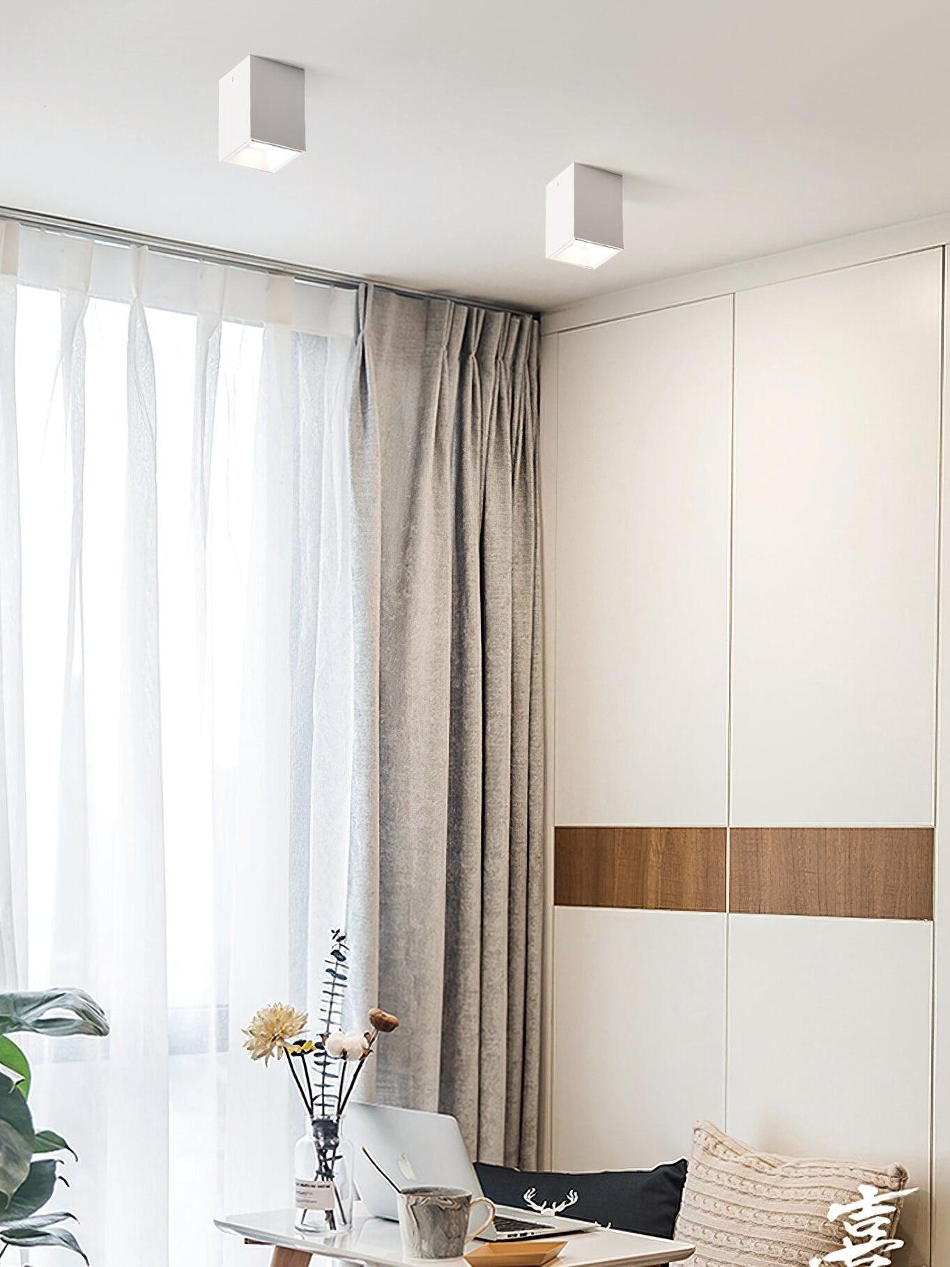 Two white ceiling spots above a seating area and laptop table beside a curtained window