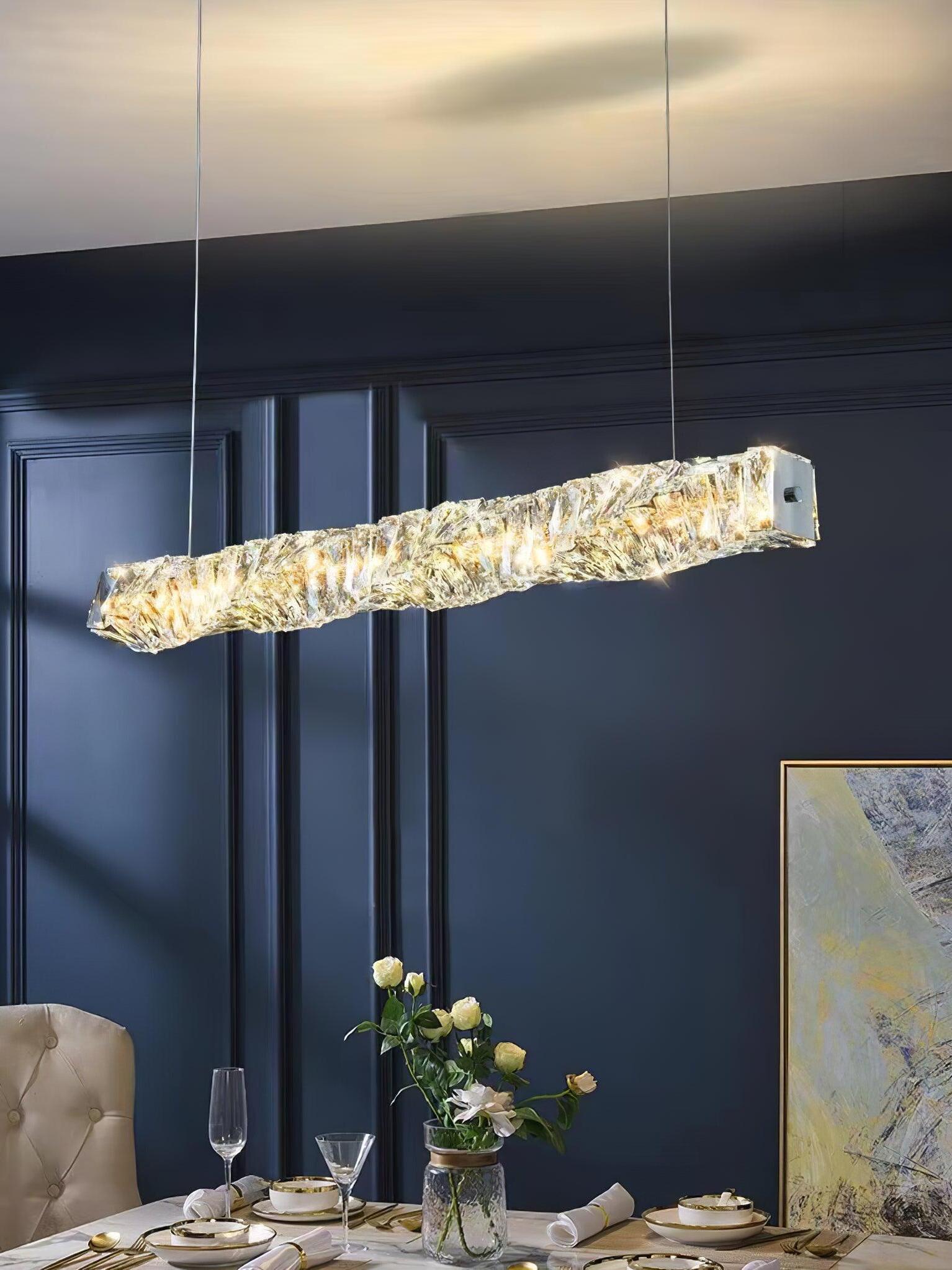 Crystal pendant with warm-looking light above a table with wine glasses and flowers against blue panelling