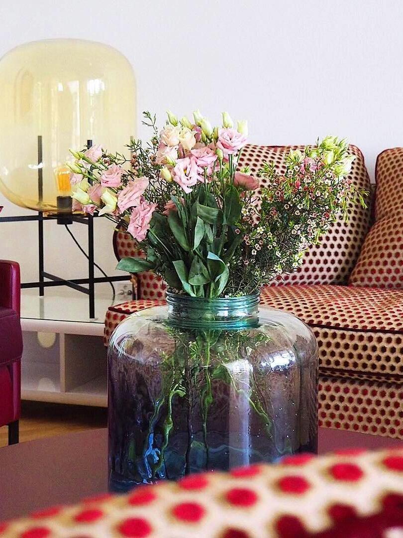 Amber glass lamp behind pink flowers and a patterned sofa.