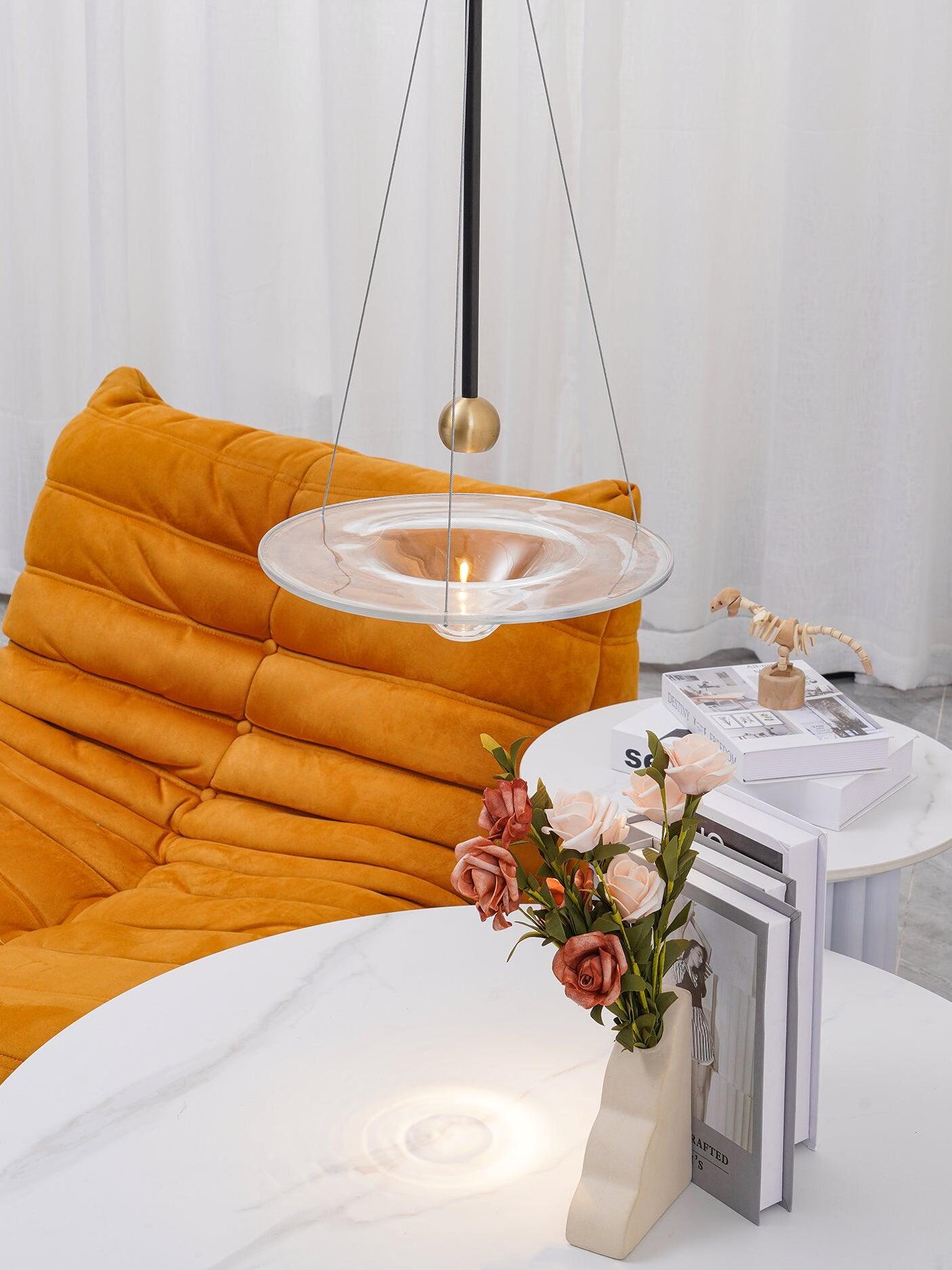 Clear disc pendant above white table and orange sofa