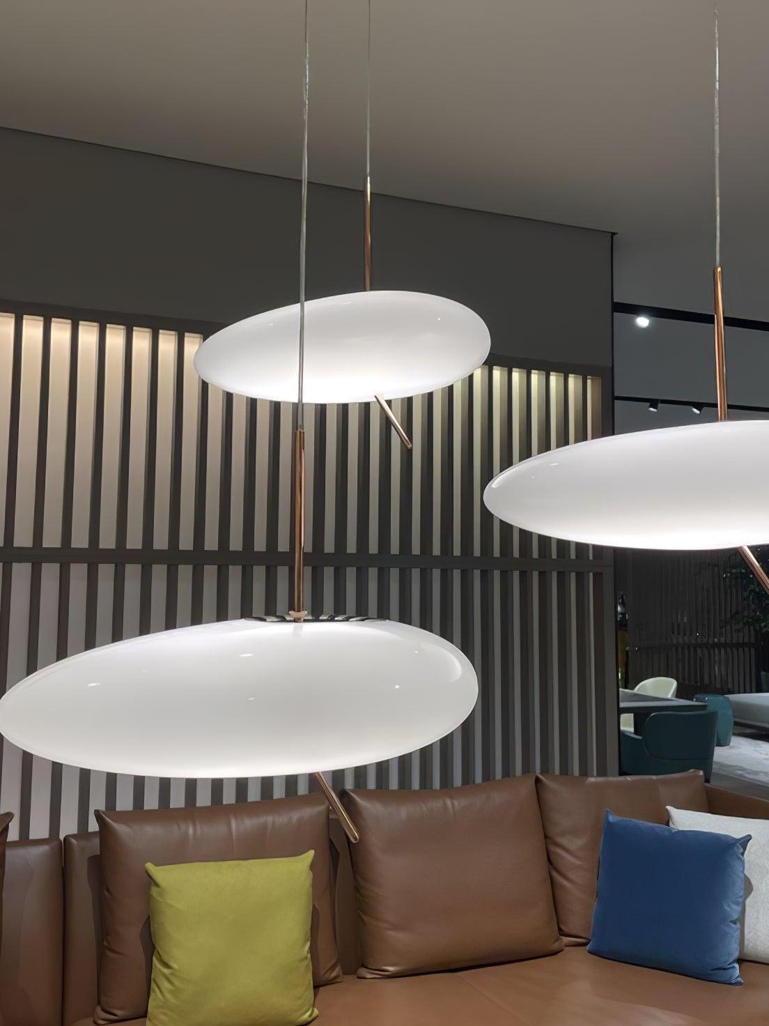 White flattened pendant shades at staggered heights above a sofa with colored cushions