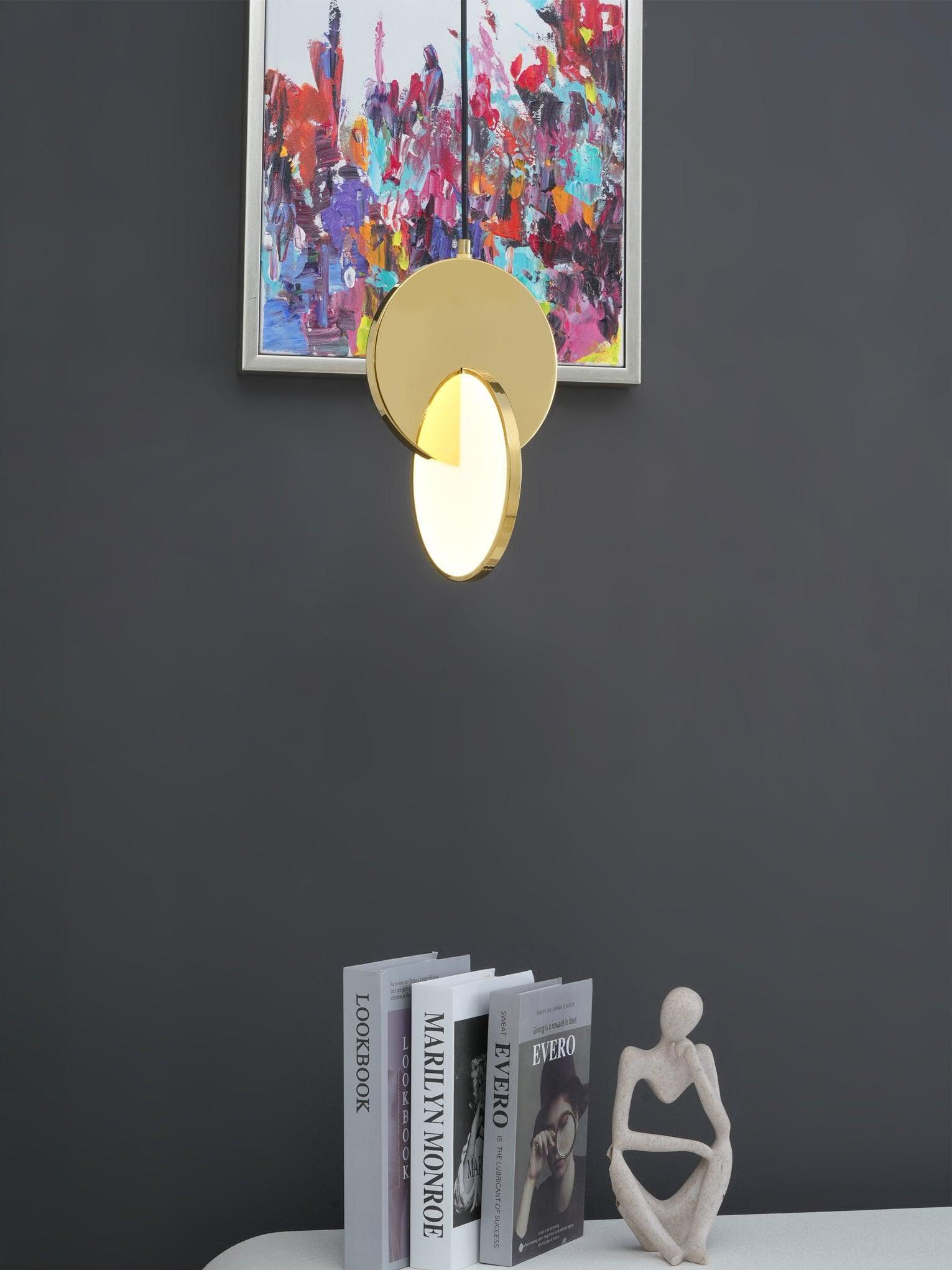 Gold disc pendant light above a console with books and a sculpture beneath a painting