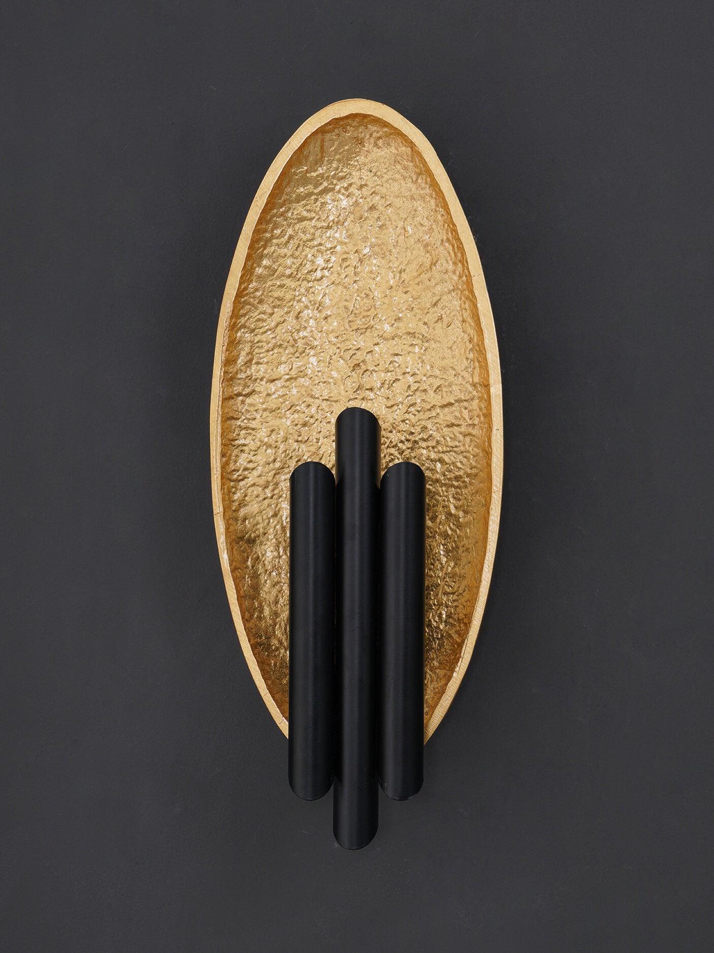 Unlit gold-tone oval panel behind three dark cylindrical pieces