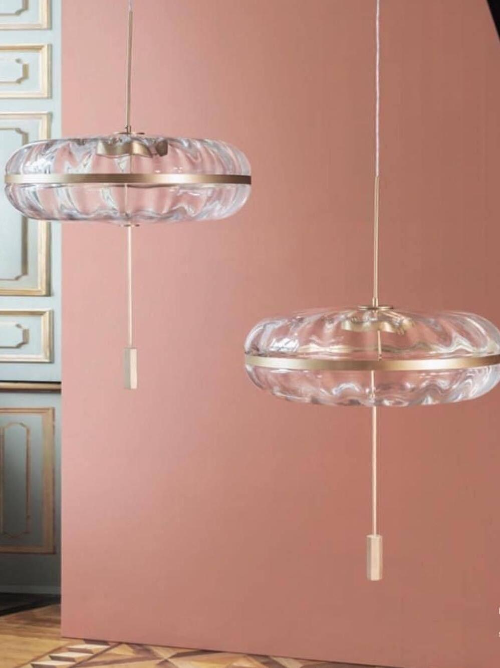 Two Jolie glass pendants against a pink wall