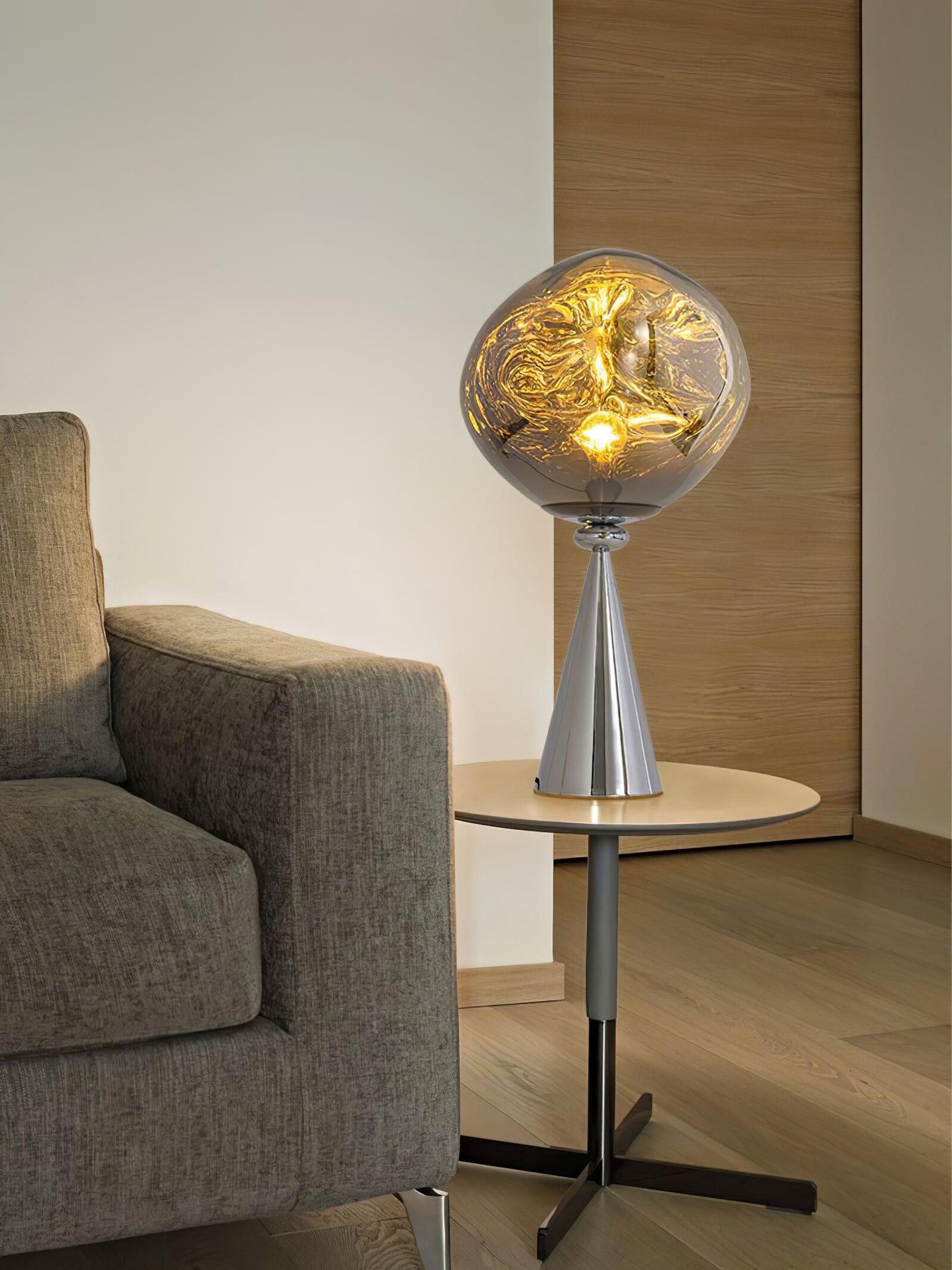 Glowing chrome globe table lamp beside a gray armchair on a round side table