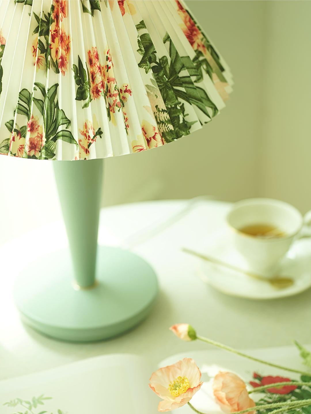 Light-blue lamp with floral shade beside cup and flowers