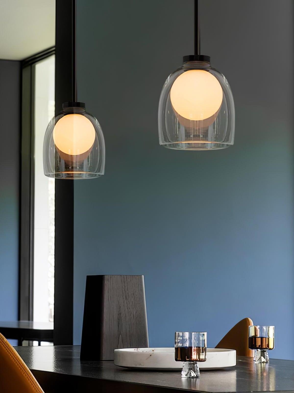 Two clear Crux pendants above a dining table beside a blue-grey wall