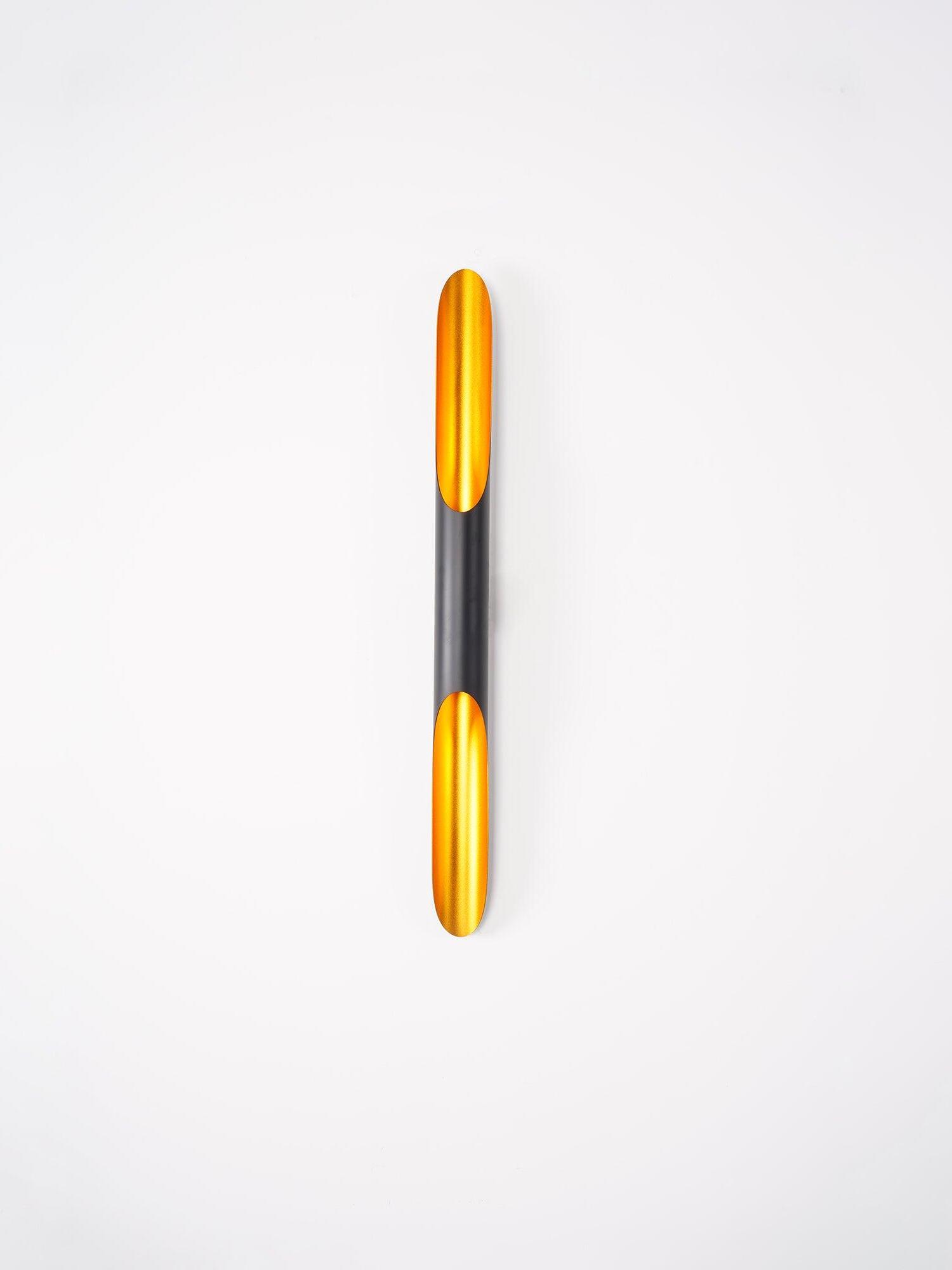 Front view of a black tubular sconce with lit gold interior on a light grey background