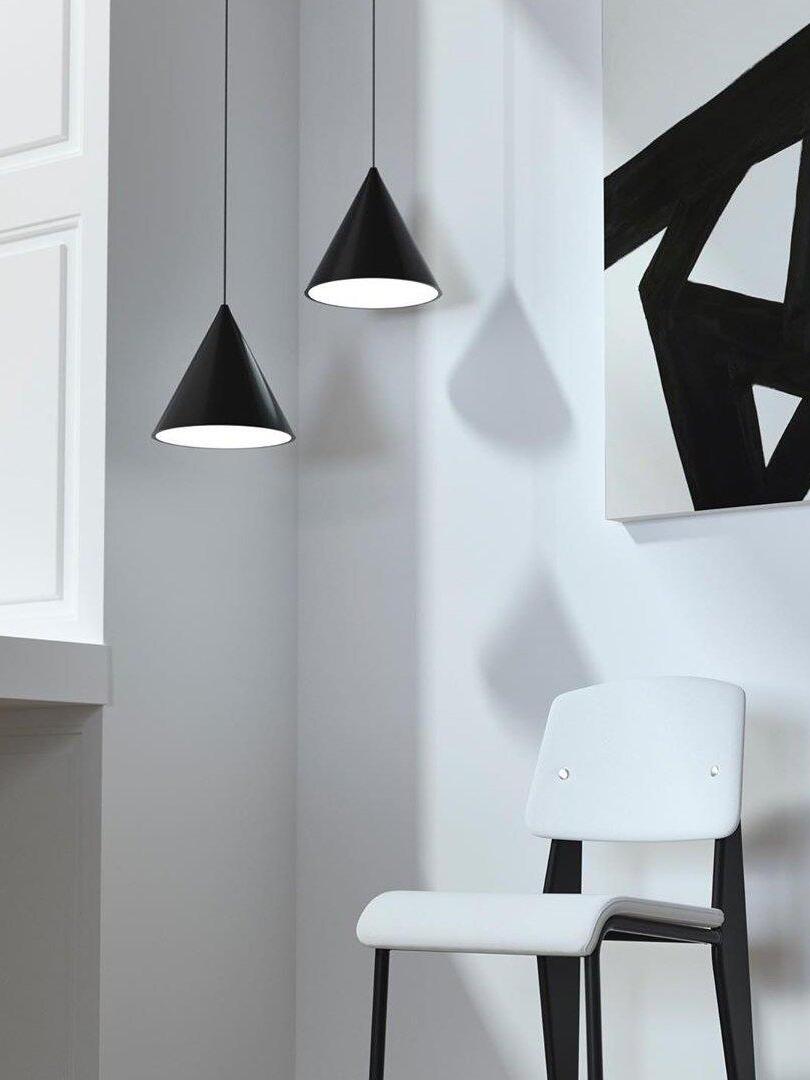 Two black cone pendants at different heights beside a white chair and black geometric wall art