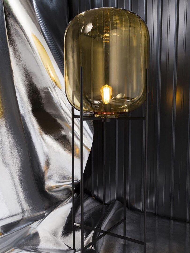 Smoke-tinted glass floor lamp in front of reflective draped material.