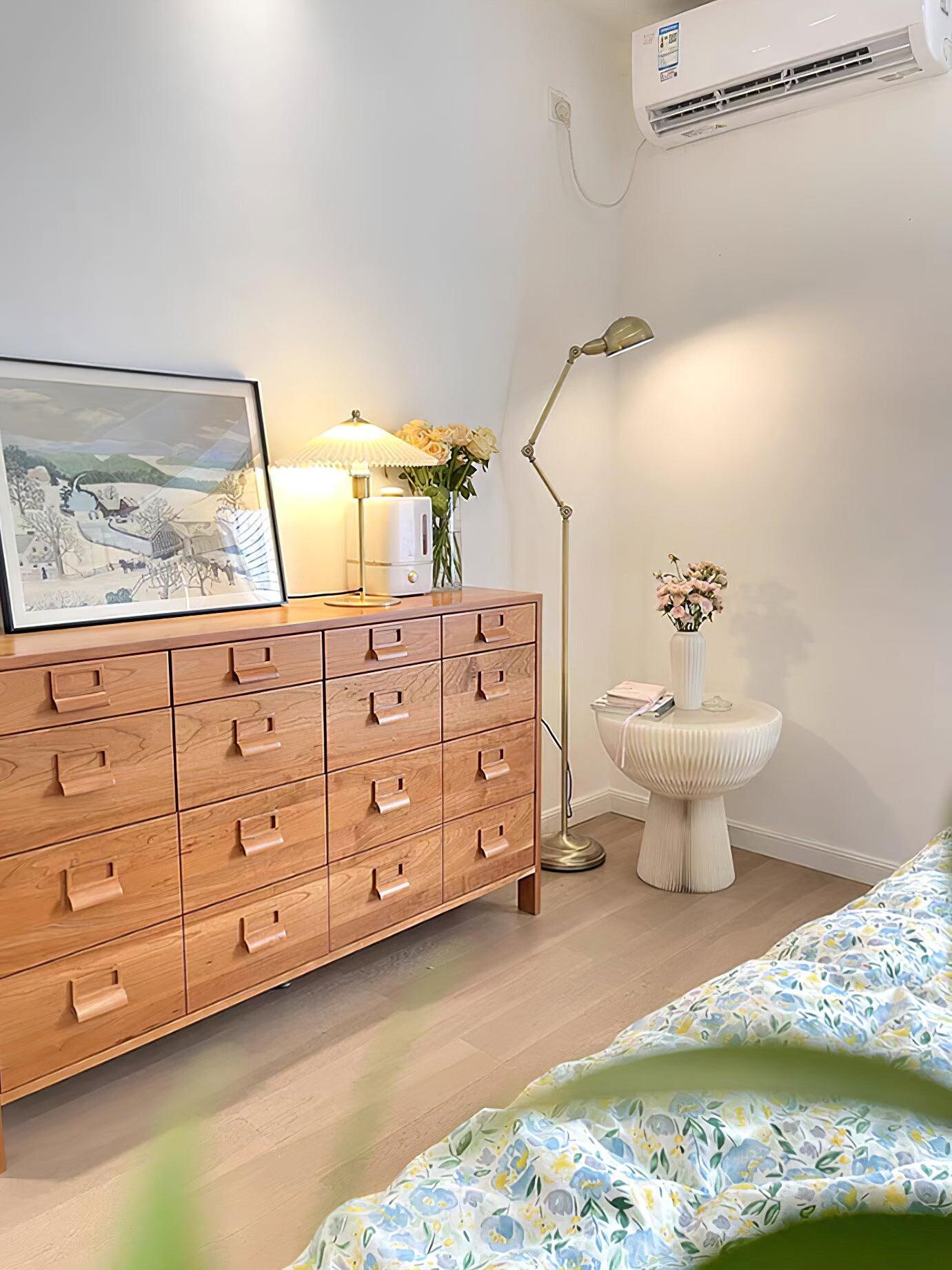 Bedroom with Perla on a wooden chest of drawers beside framed art, a plant and a separate floor lamp