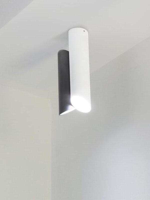 Illuminated white and black tubular ceiling light beside a wall corner