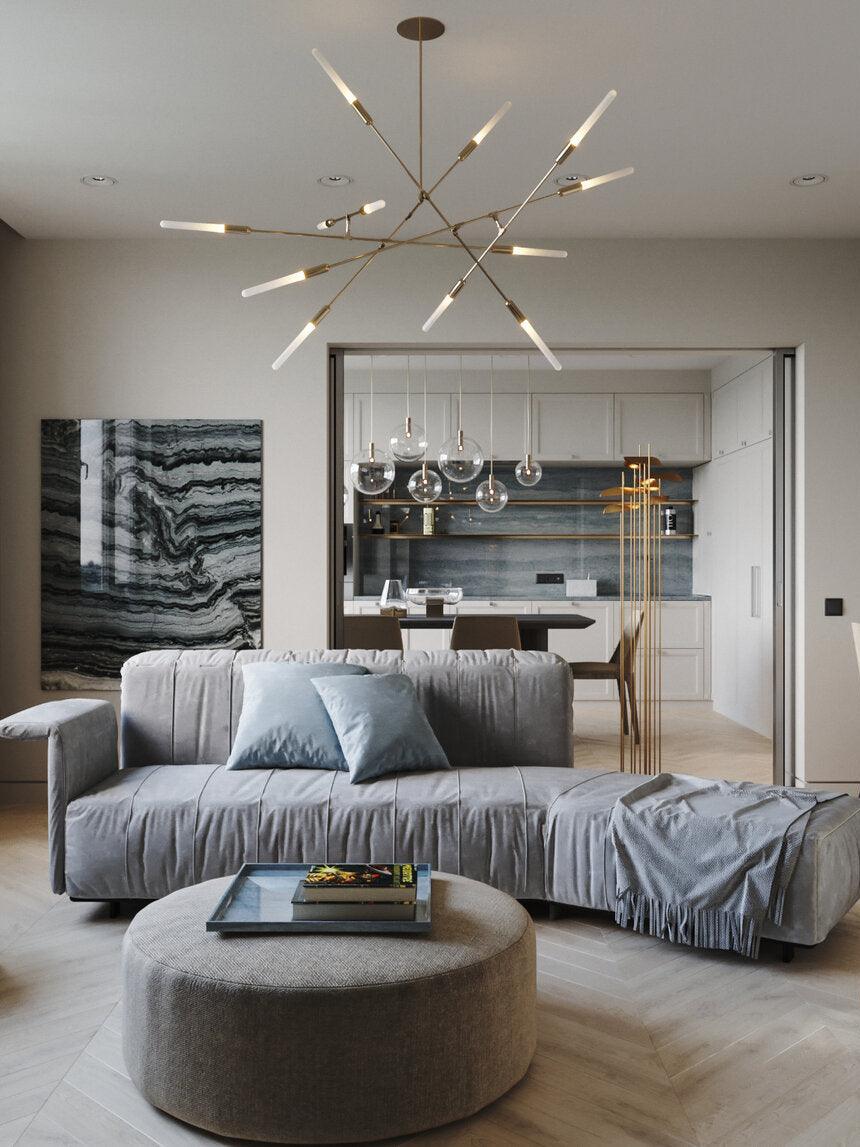Gold-coloured branch chandelier above a grey sofa in an open living and kitchen space