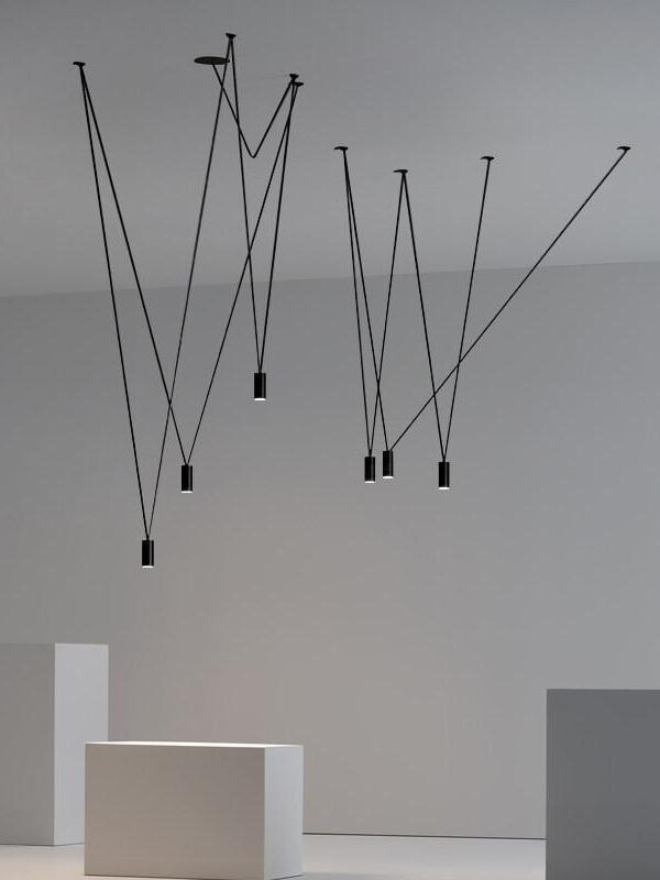 Six black cylindrical terminals hanging at different heights in a crossing linear arrangement in a gray room