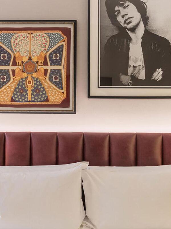 Pink upholstered headboard beneath two framed pictures with white pillows in front