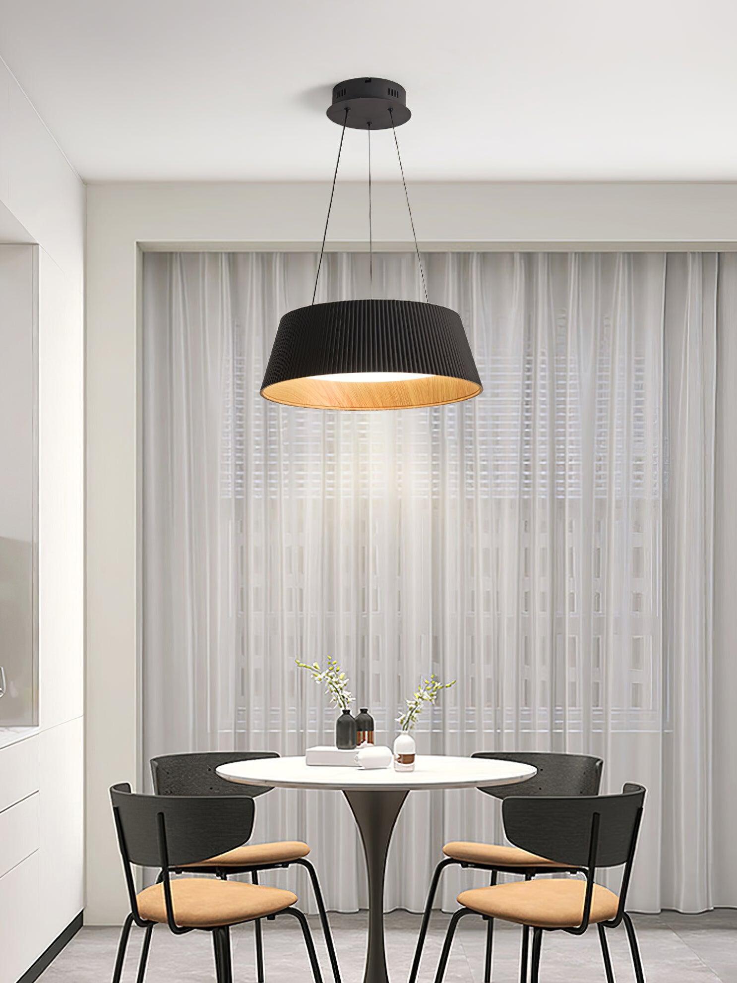 Black ribbed pendant above a white round dining table with four black chairs, flowers and white curtains