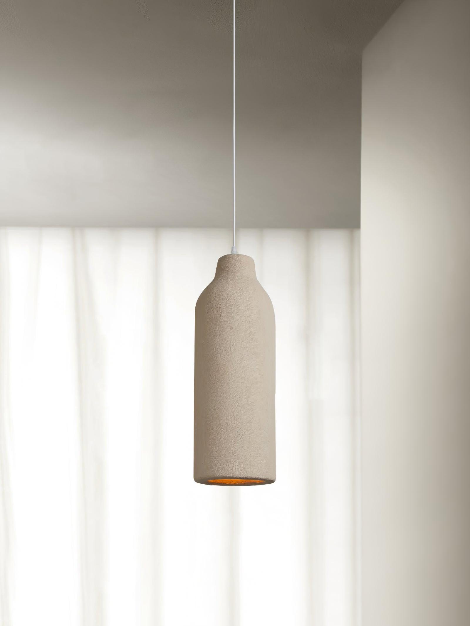 Narrow bottle-form textured pendant with short neck and warm-looking opening against pale sheer curtains