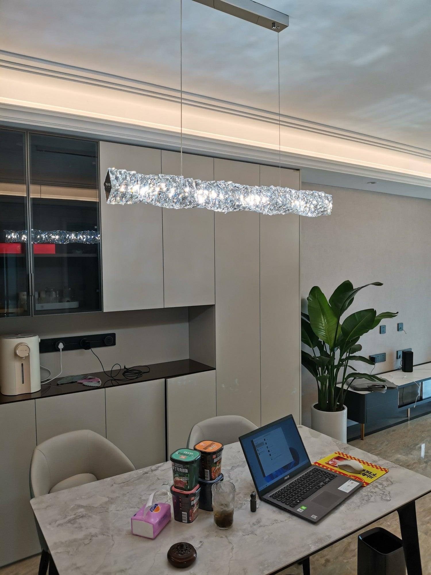 Long crystal pendant above a marble table with a laptop beside a kitchen and leafy plant
