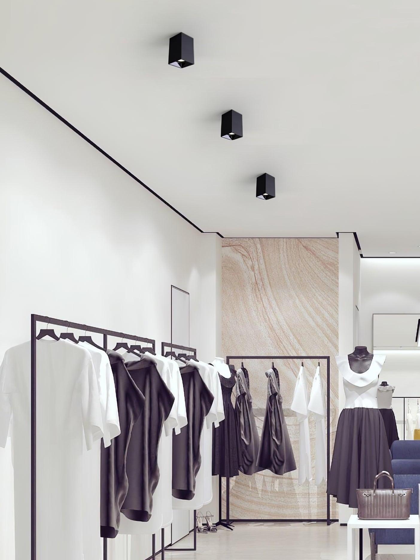 Three black ceiling spots above clothing rails and a mannequin in a display area
