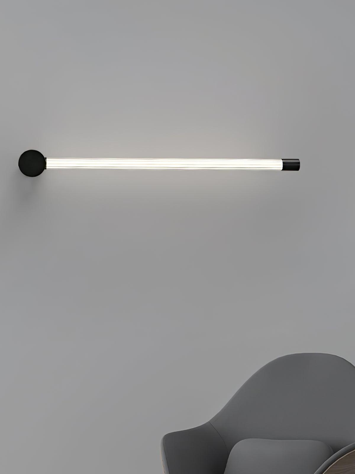 Black single-tube wall light mounted horizontally above the edge of a gray chair