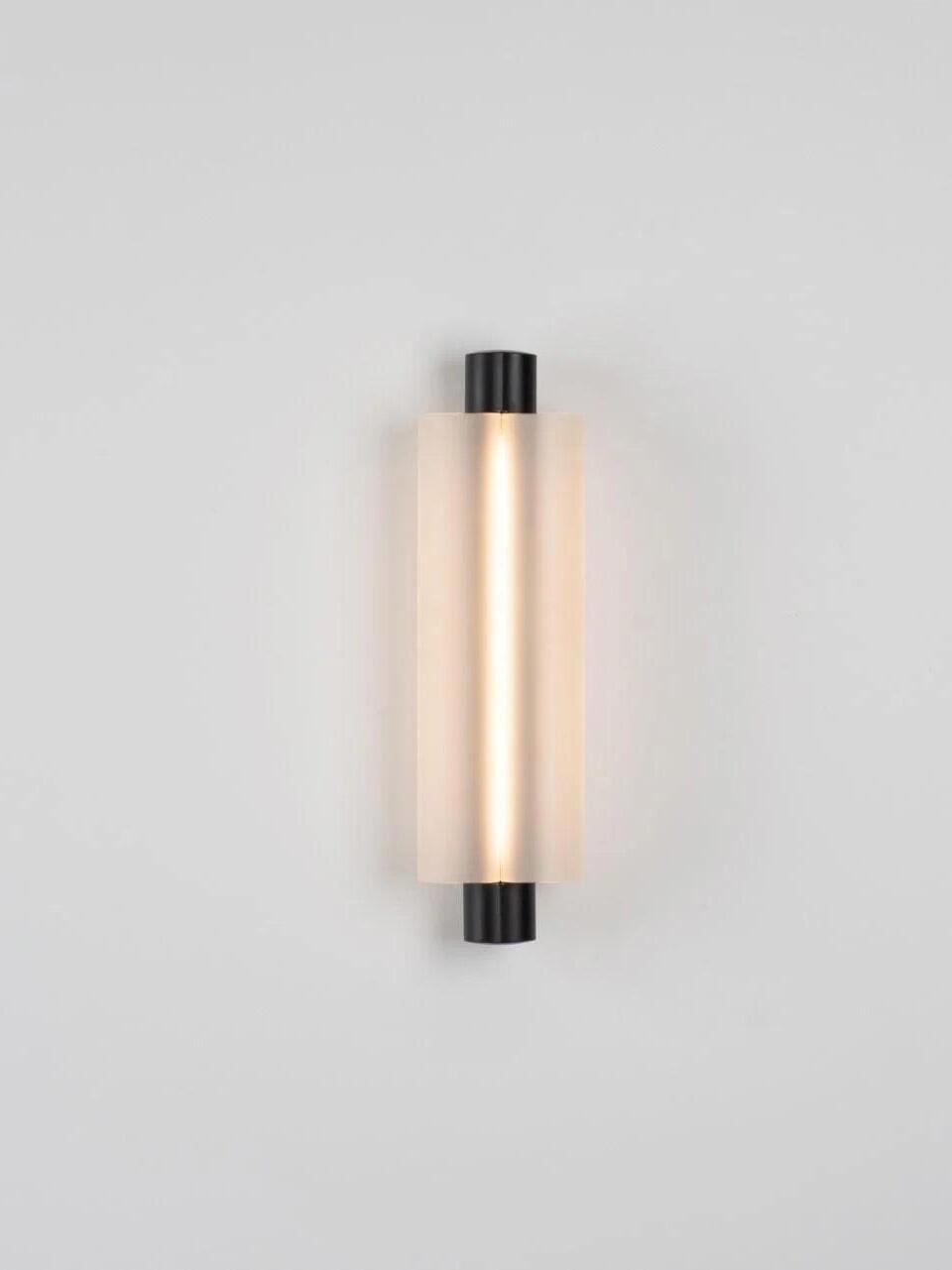 Black-ended vertical light with pale translucent shade alone on wall