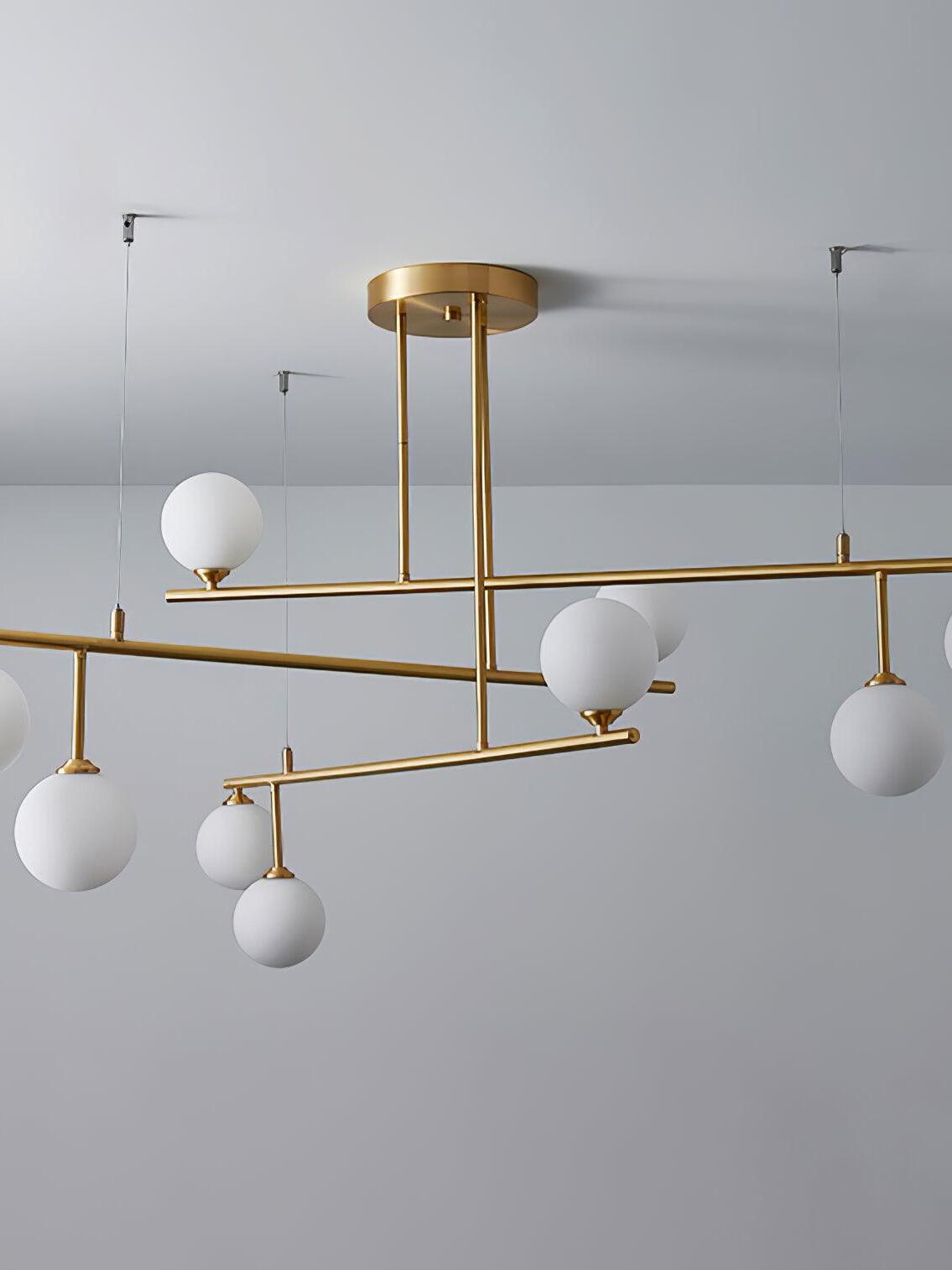 Unlit Arteriors chandelier showing white globes at different levels around the brass-tone frame