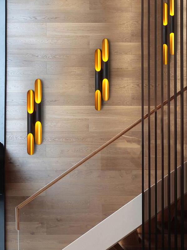 Twin-tube black and gold wall sconces along wood-panelled stairs beside a wood handrail and black balusters