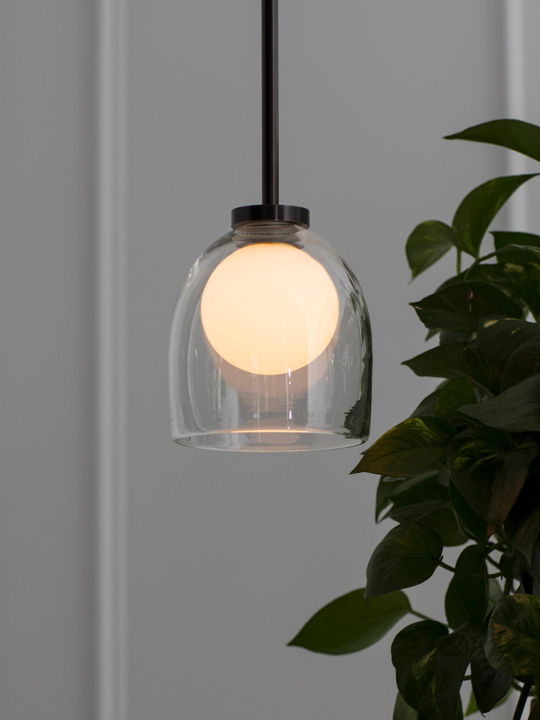 Close view of the glowing sphere inside a clear Crux bell shade beside green leaves