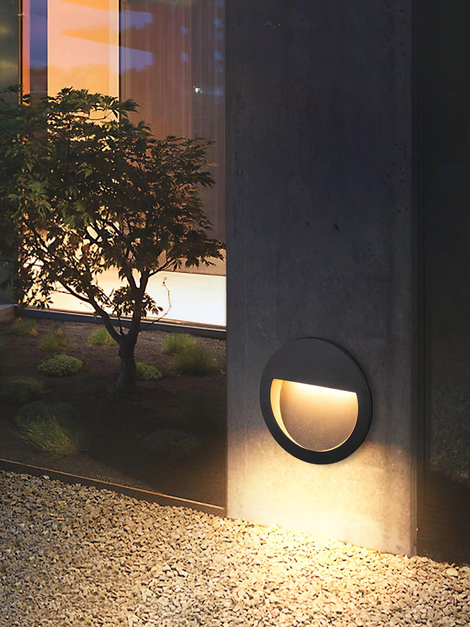 Round wall light beside tree and gravel at dusk