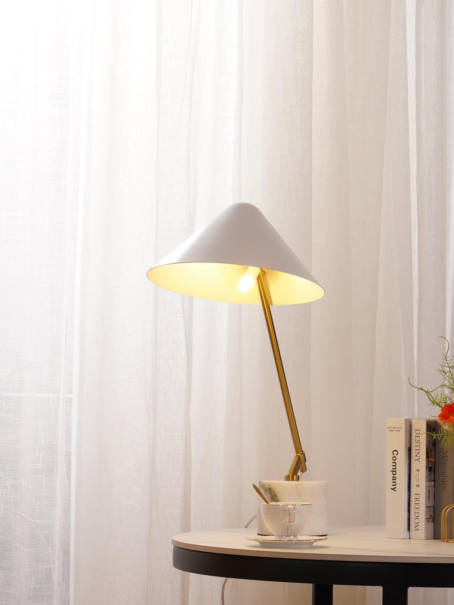 Lit white shade and gold-tone arm on a table with a cup and upright books