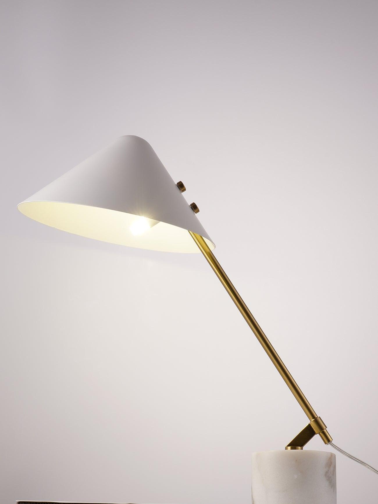 Lit angled white shade and gold-tone arm with cylindrical patterned base partly cropped