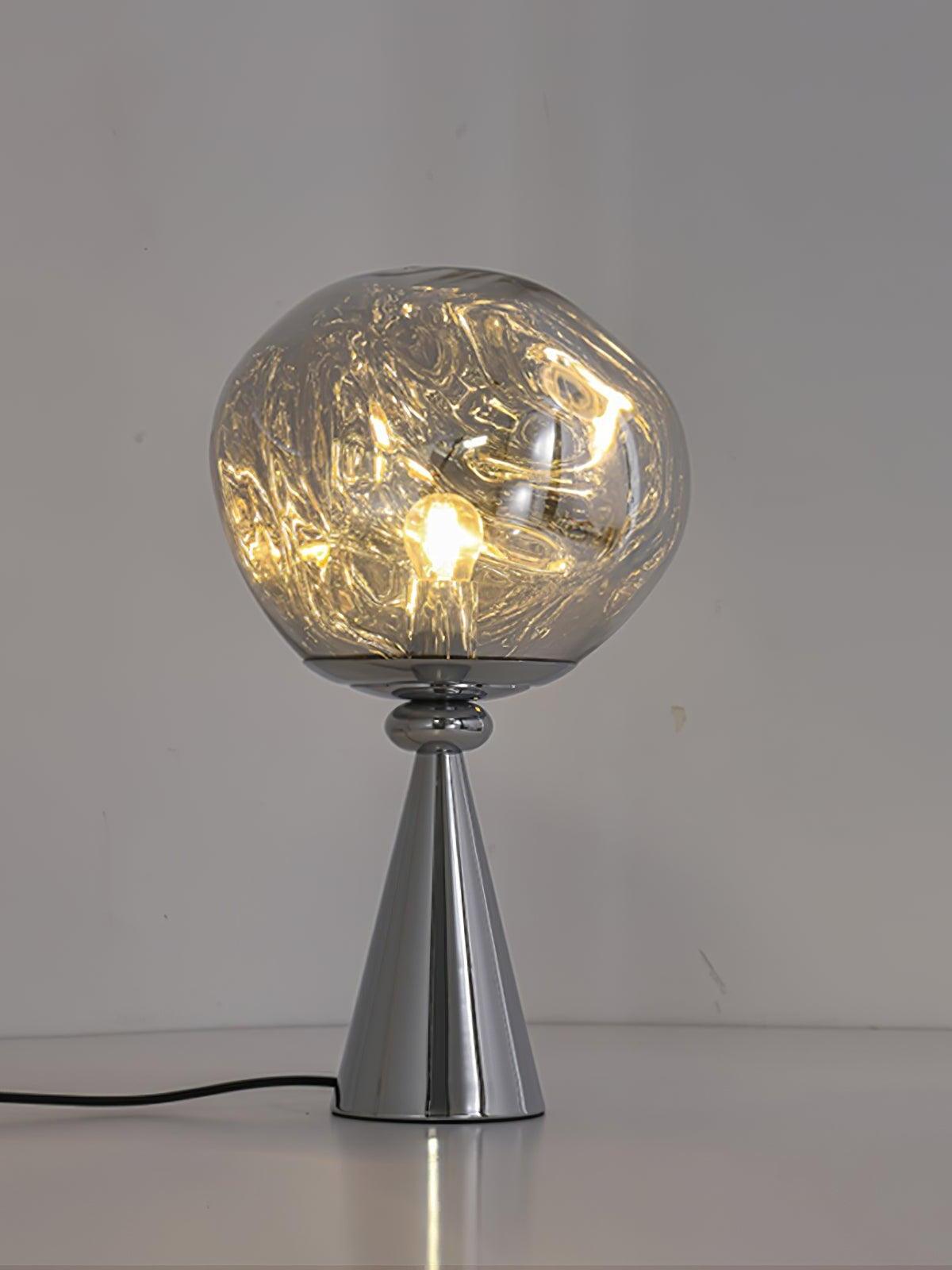 Glowing irregular globe on a chrome cone base with a cord resting on a white table