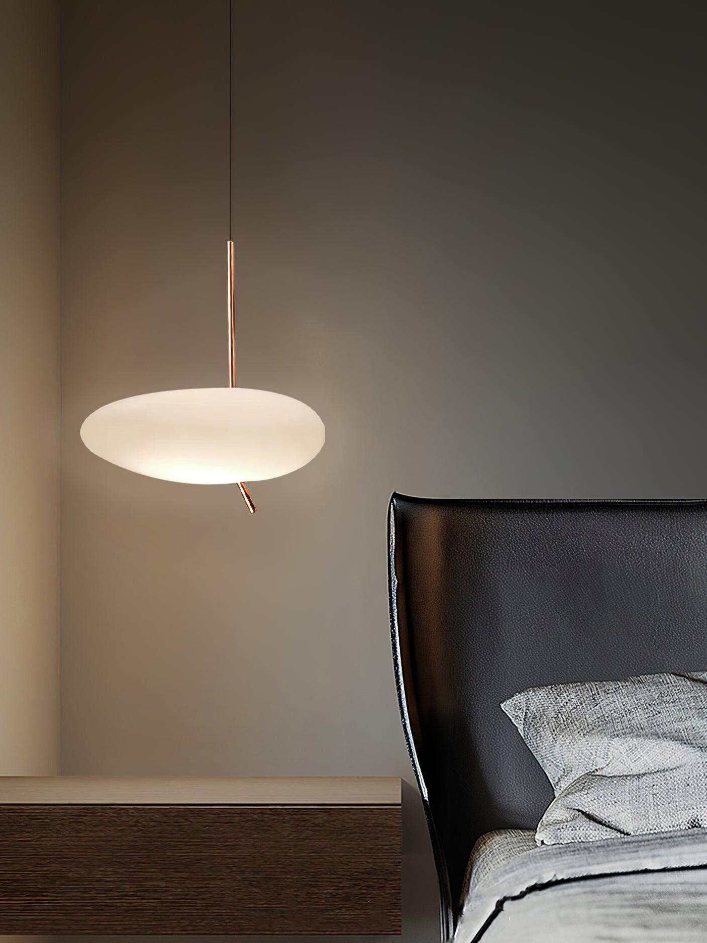 Glowing white pendant suspended beside a bed with a dark headboard