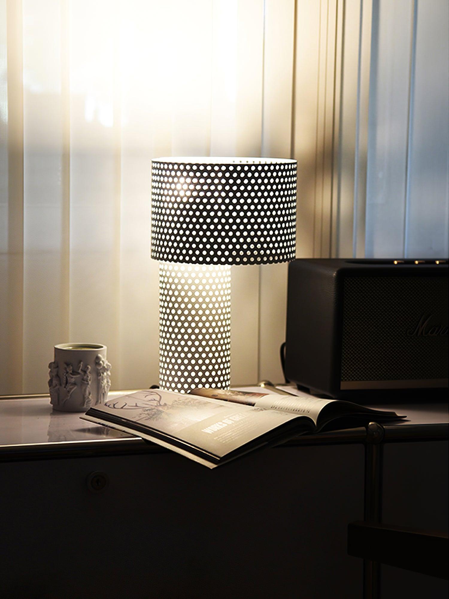 Lit perforated lamp beside mug on dark desk