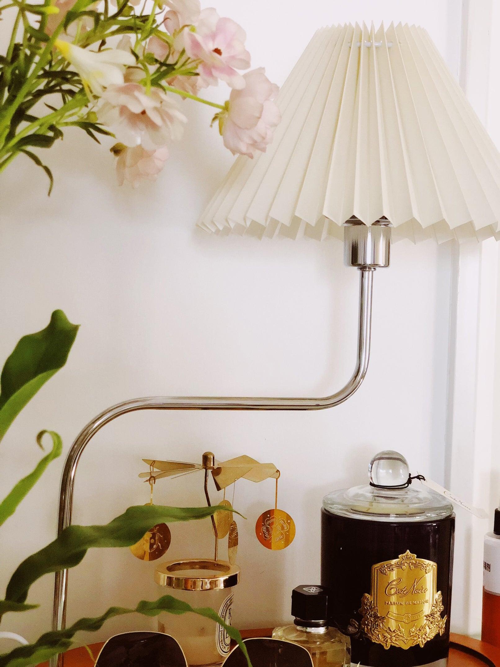 Pale pleated lamp near flowers and glassware