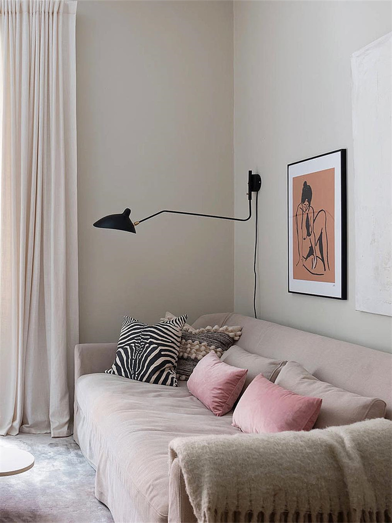Black single-arm wall light above a pale sofa with pink zebra cushions, framed art and a cord running down the wall
