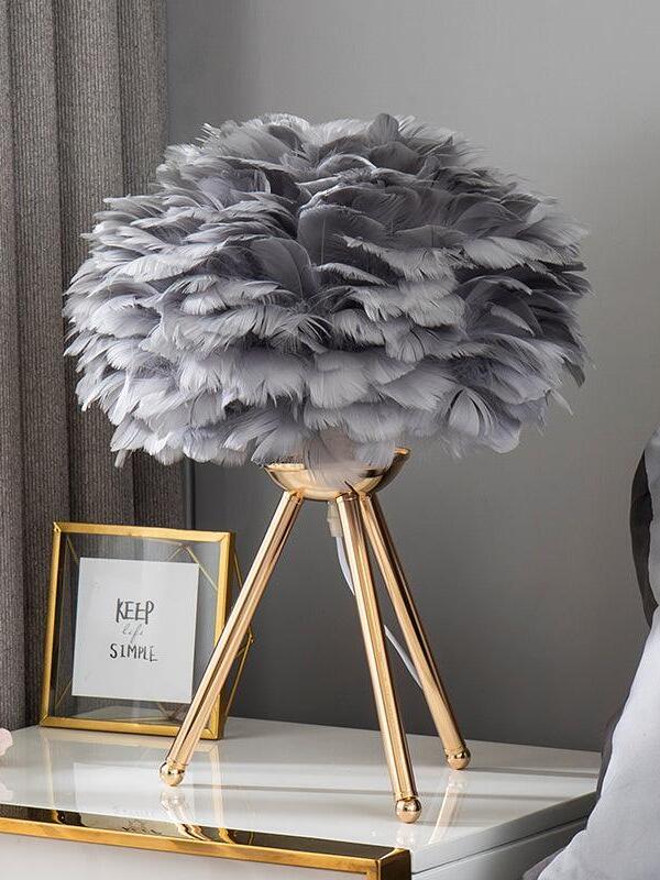 Grey feather lamp on gold tripod atop dresser