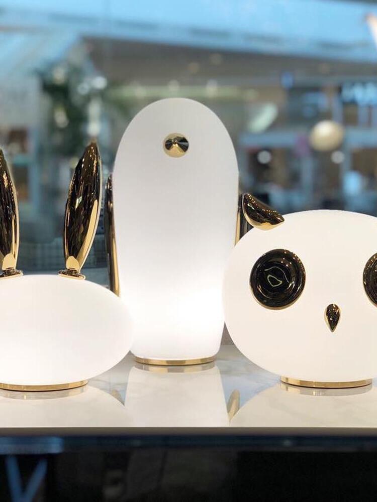 Rabbit, penguin and owl glass lamps grouped on reflective table