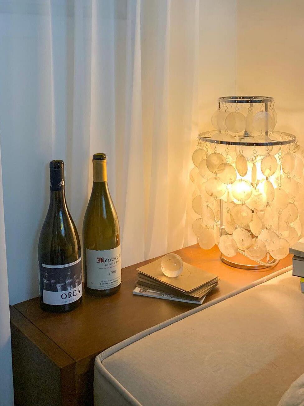 Shell table lamp on wood surface with wine bottles and book