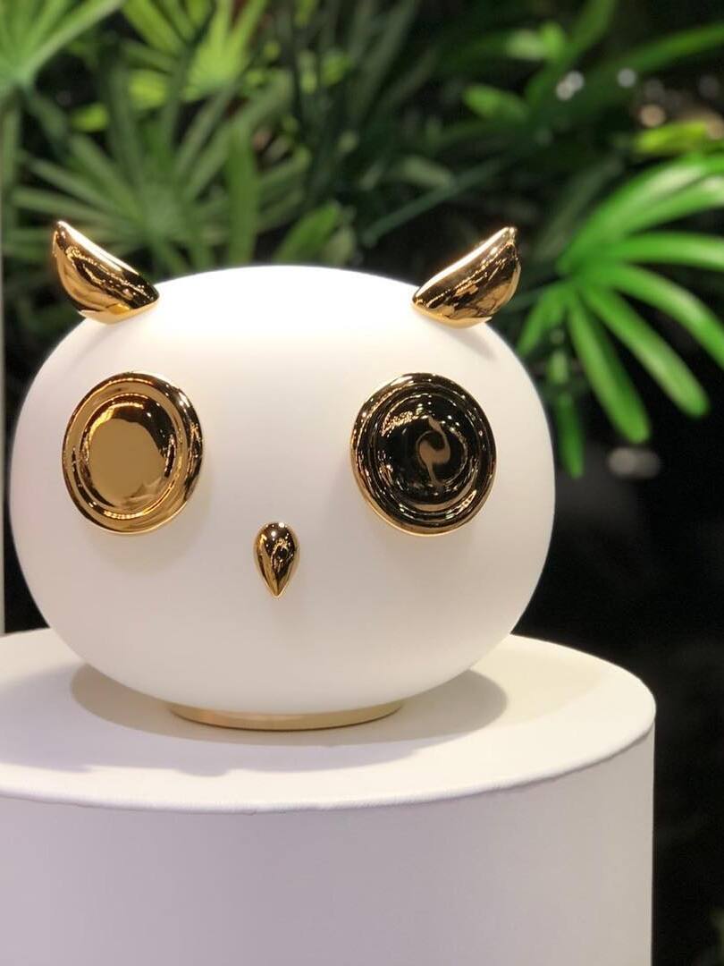 Close owl globe with reflective gold-tone eyes and pointed ears before plants