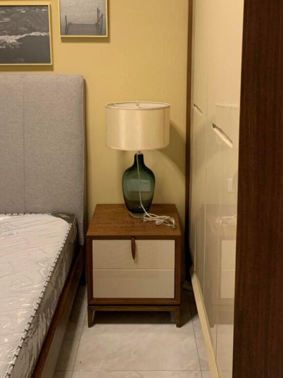 Bedside lamp with pale drum shade and cord on cabinet