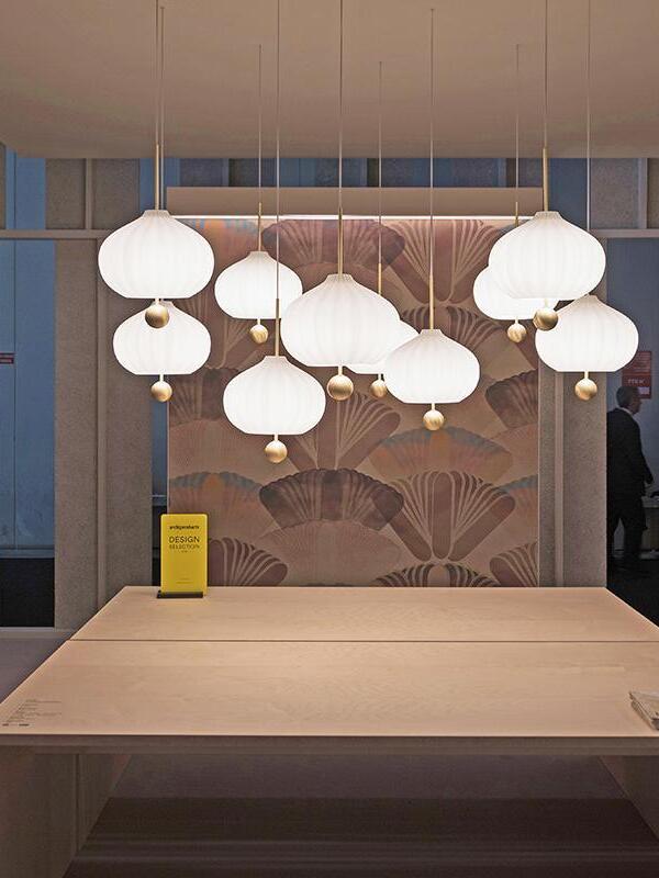 Cluster of white fluted pendants with brass balls at varying heights over a wooden table and floral artwork