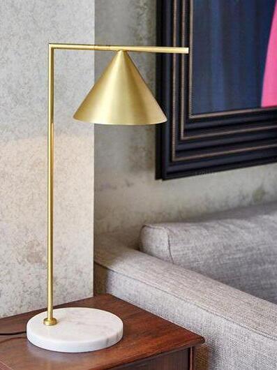 Gold-tone cone lamp on wooden side table beside grey sofa