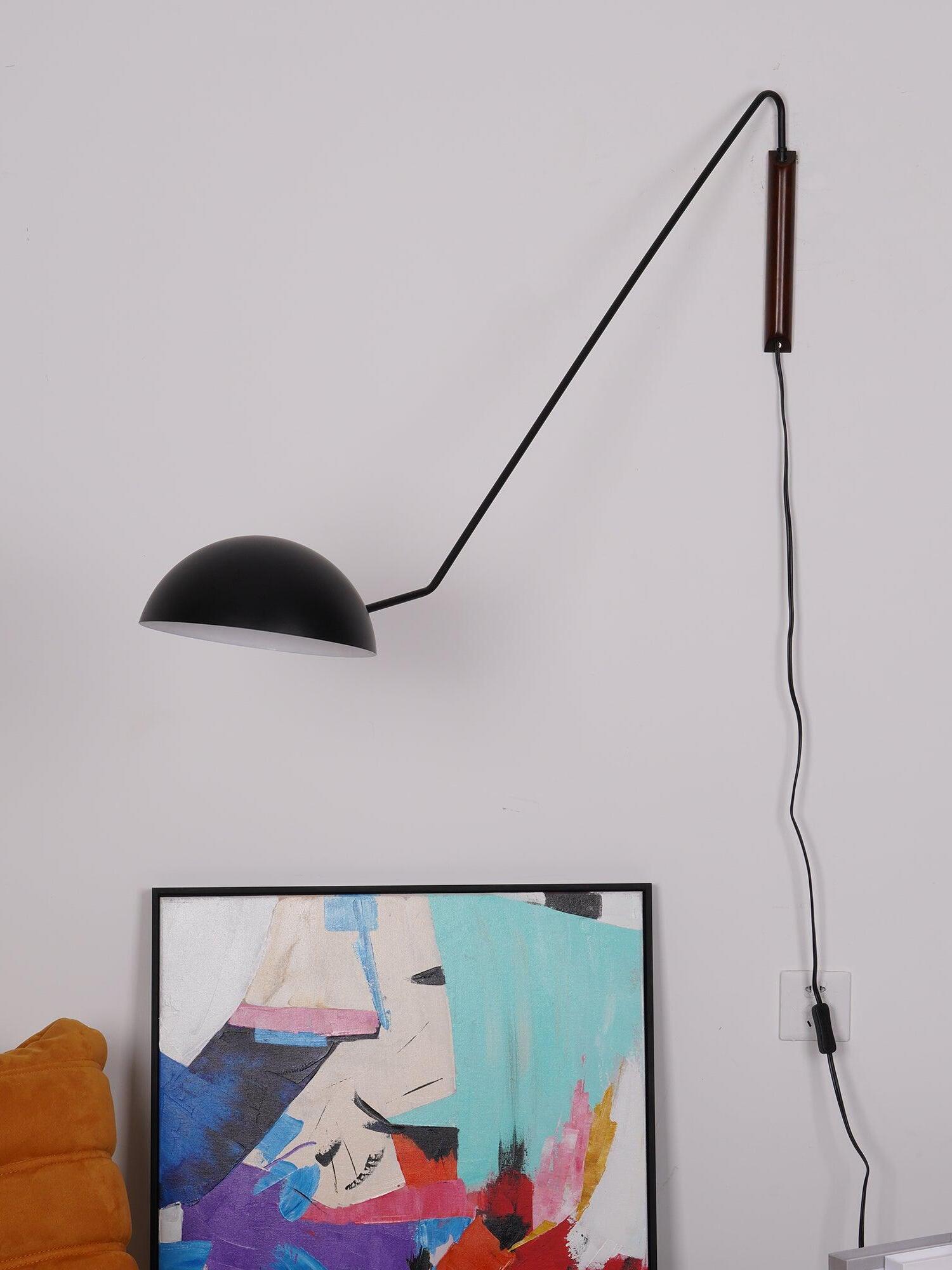 Black dome with white interior on an angular arm and dark wooden mount, above abstract art beside an orange sofa
