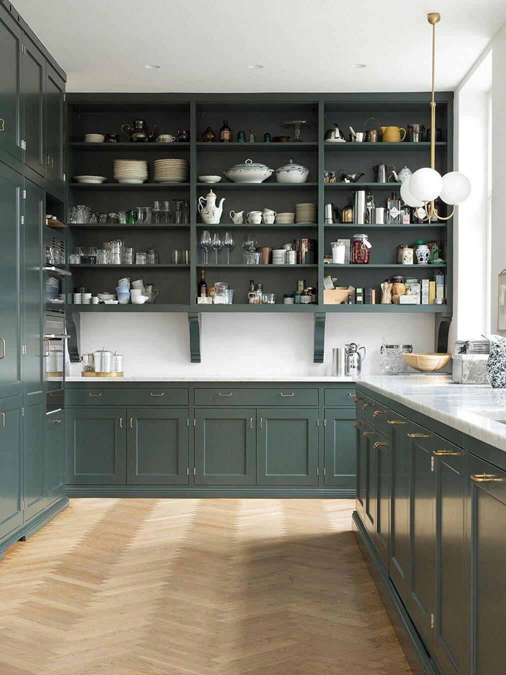 Three-globe brass pendant beside a counter in a dark green kitchen
