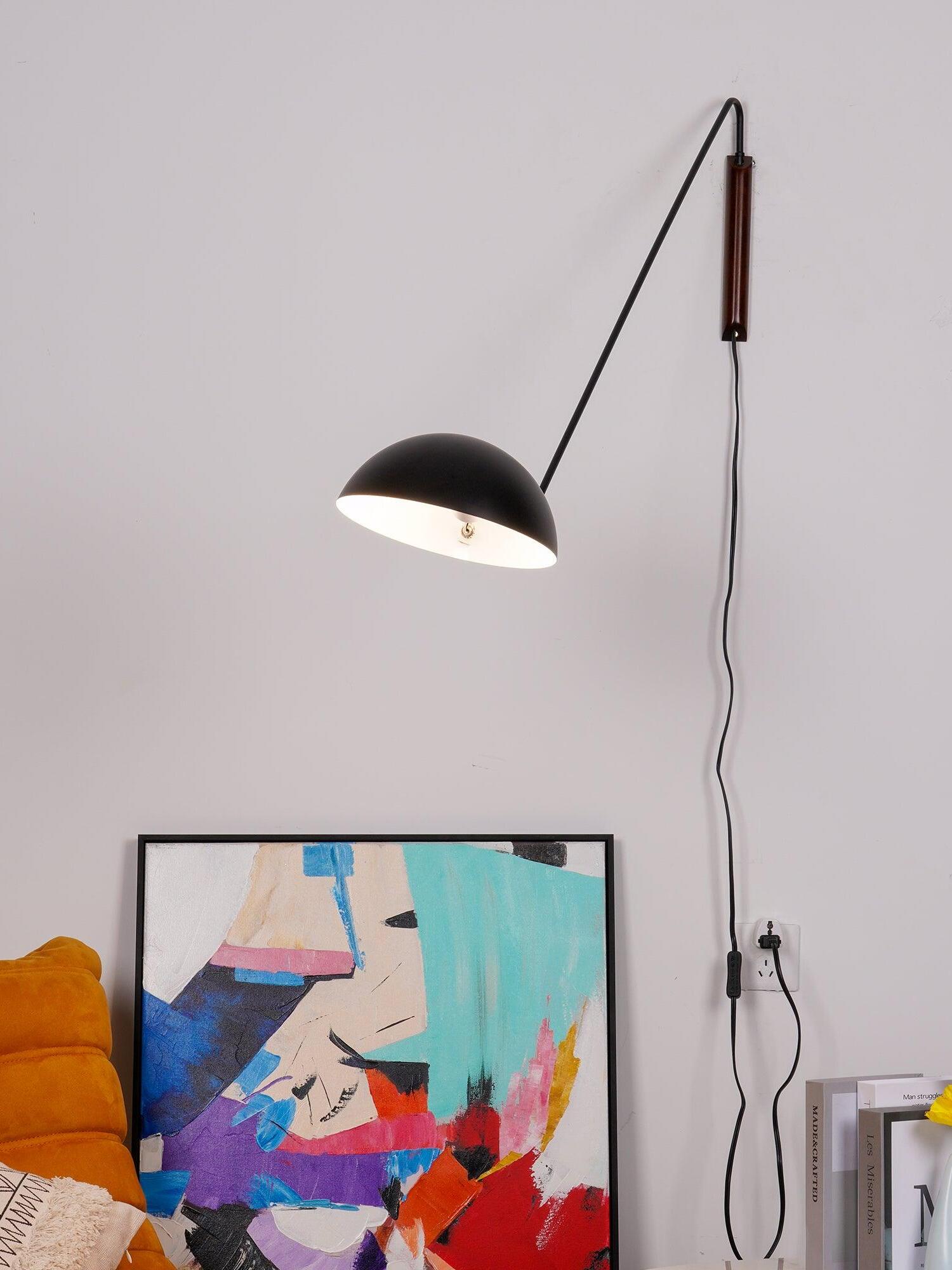 Lit black dome wall lamp with dark wooden mount and switched cord plugged into an outlet beside abstract art