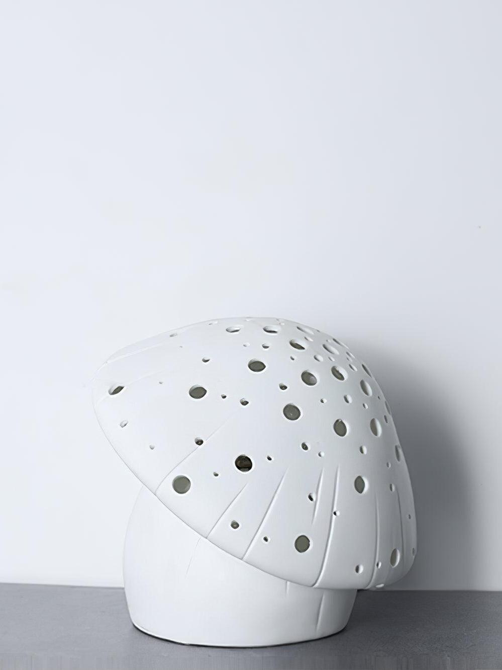 Unlit white Fungo lamp with circular openings and curved grooves on a dark surface