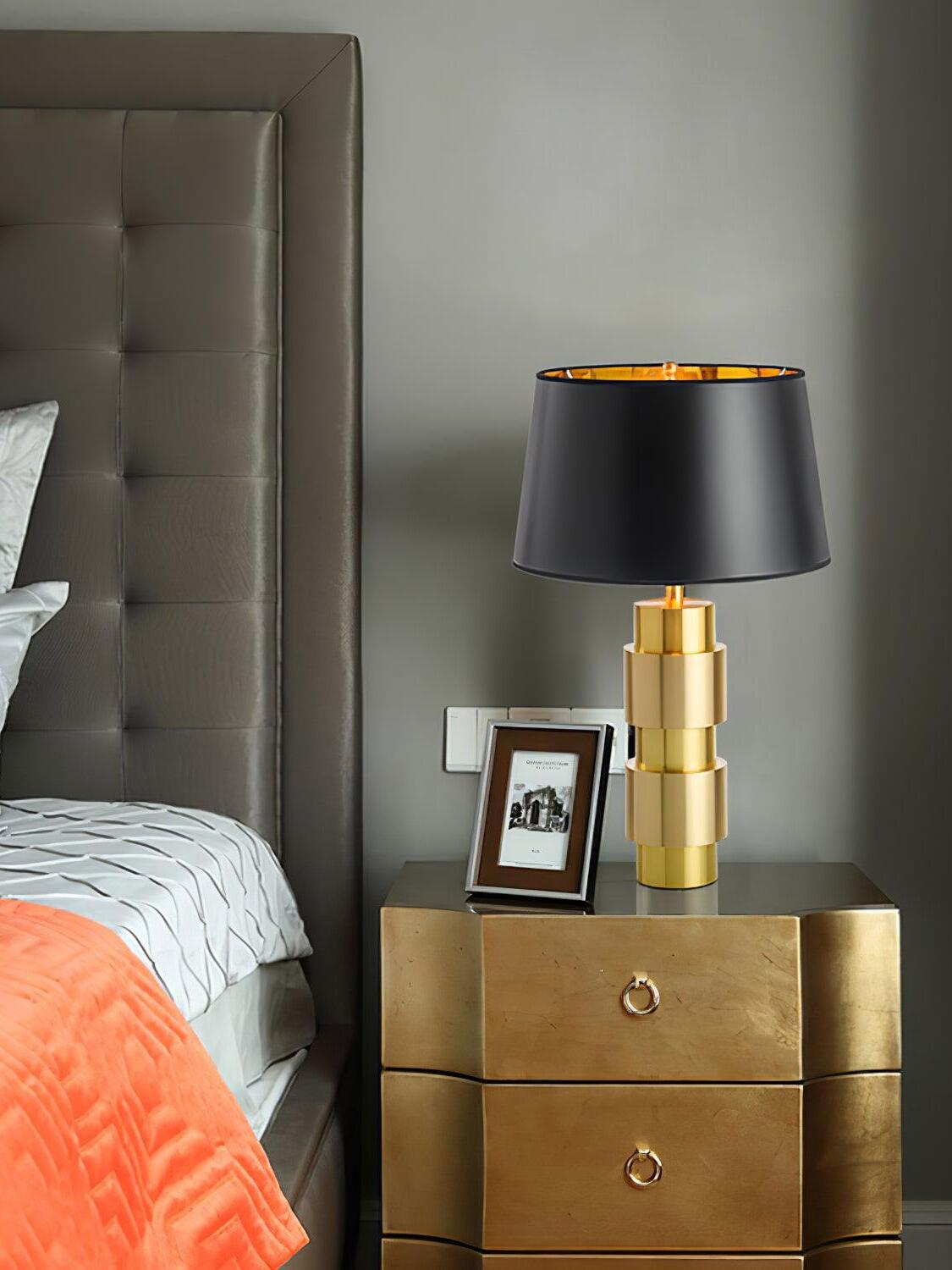 Jean lamp beside a bed on a gold-tone drawer cabinet with a framed photograph