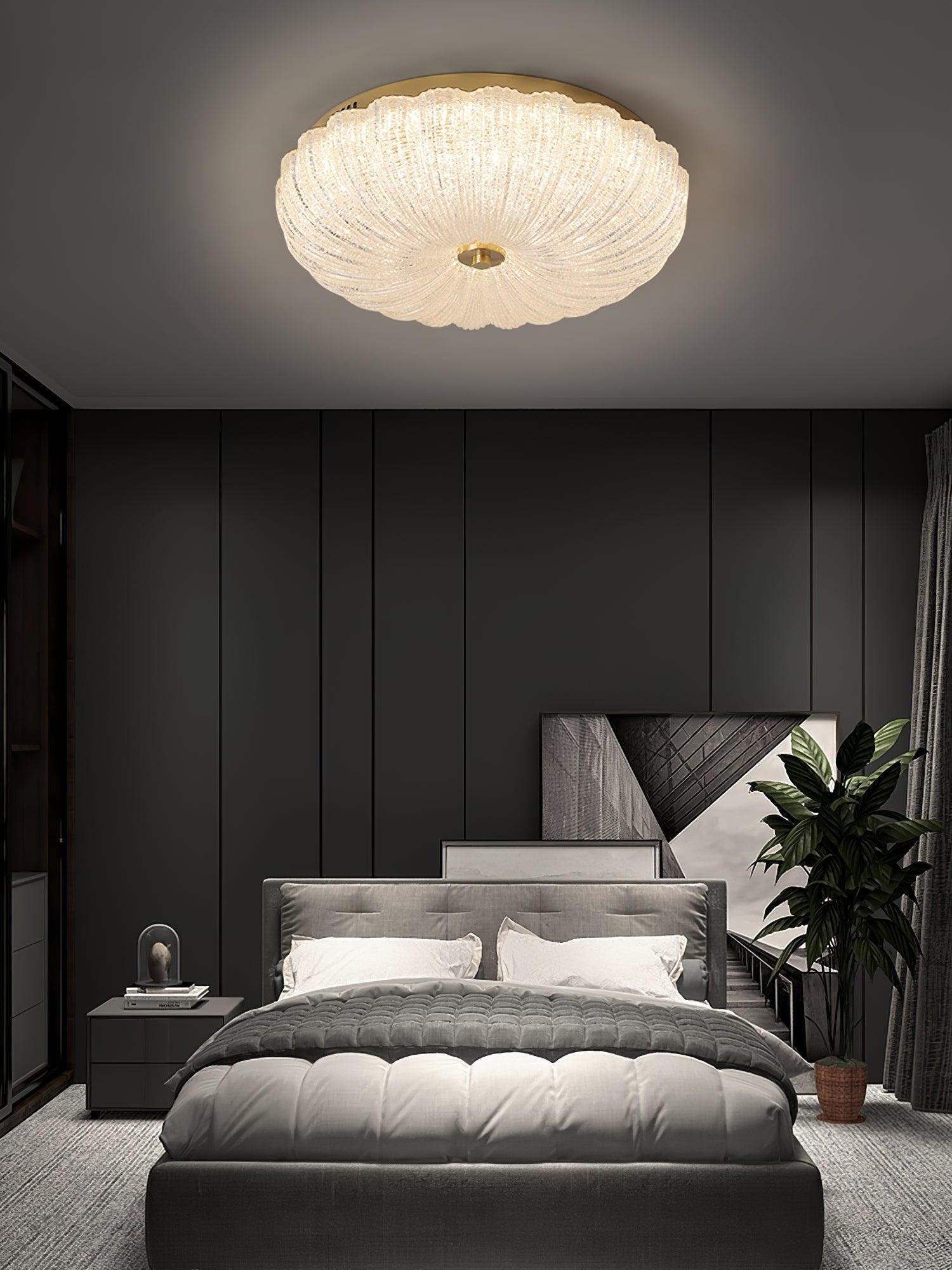 Lit scalloped glass ceiling light above a gray upholstered bed with dark paneled walls and a plant