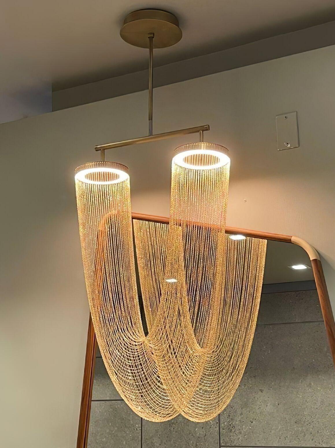 Illuminated U-shaped chain chandelier beside a leaning mirror